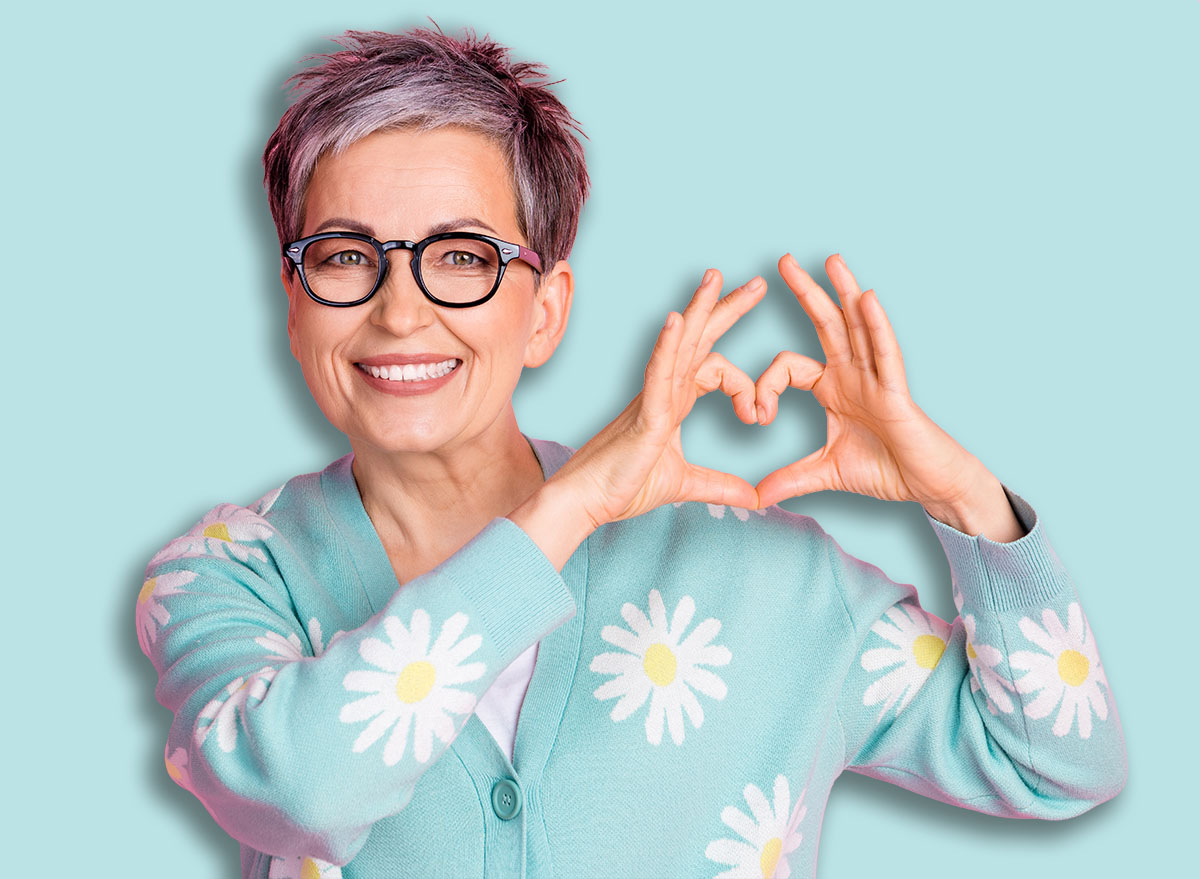 Charming,Senior,Woman,Smiling,In,Colorful,Cardigan,Making,Heart,Gesture