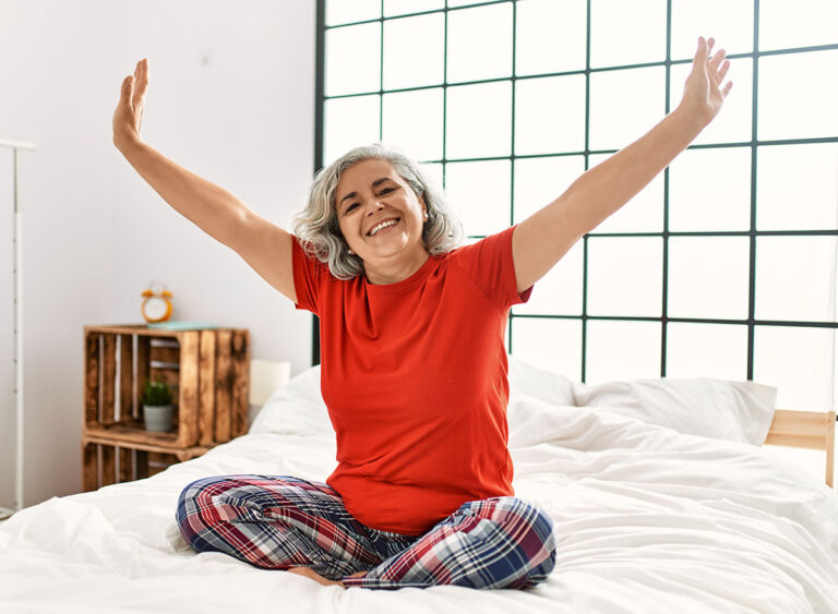 Middle,Age,Grey-haired,Woman,Smiling,Happy,Sitting,On,The,Bed