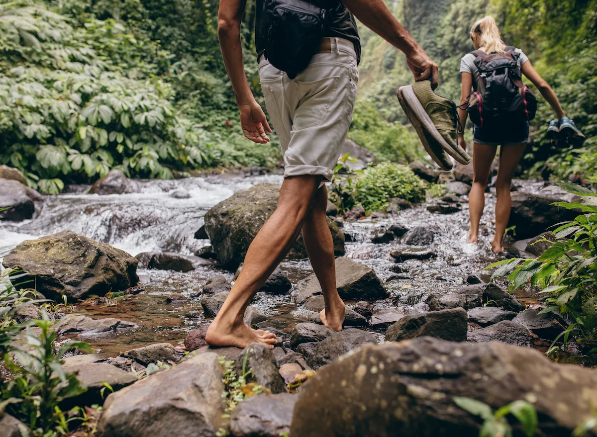 Low,Section,Shot,Of,Man,And,Woman,Crossing,The,Stream